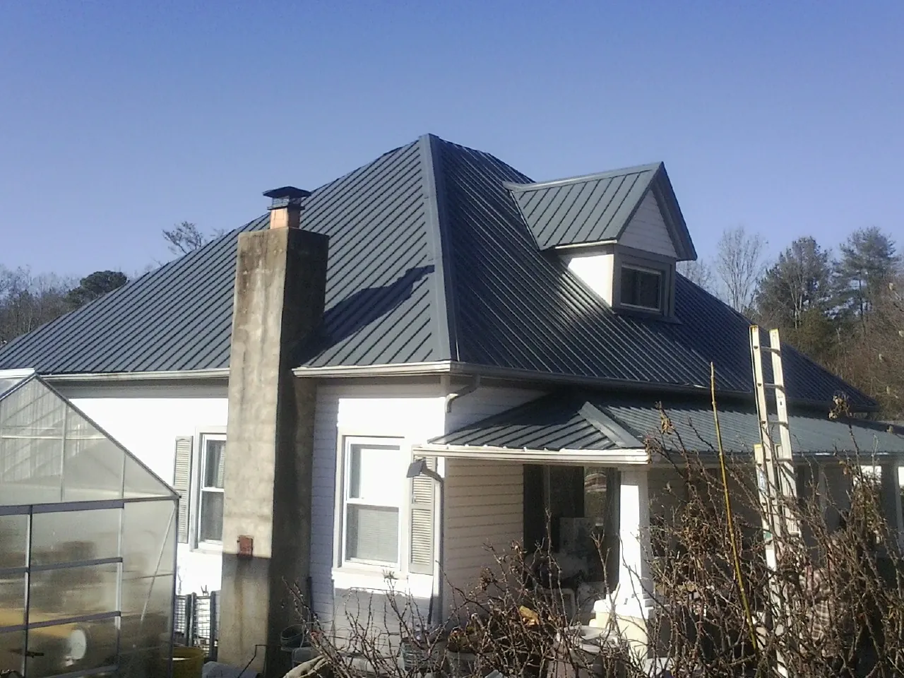 Dark blue standing seam metal roof on a white farmhouse with dormer — Slate & Tile Roof Repair by Roofing Brothers in Antelope