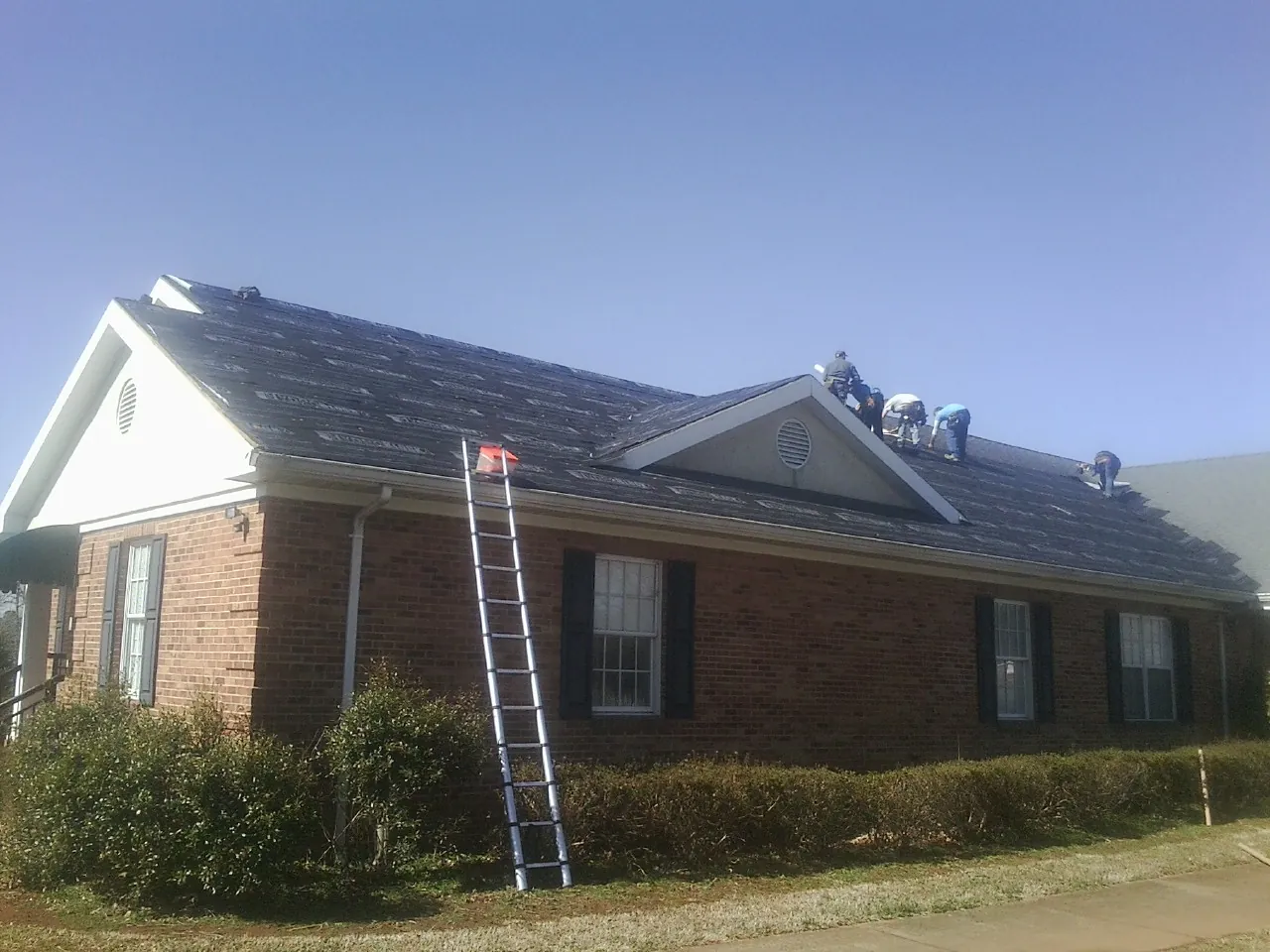 Crew tearing shingles off a brick ranch roof with a ladder set — Metal Roof Repair work by our crew in Antelope