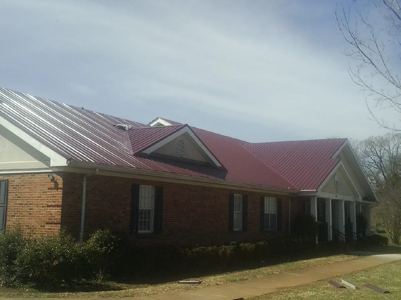 Red metal roof with gabled entries on a long brick building, from a Hail Damage Roof Repair job in Antelope