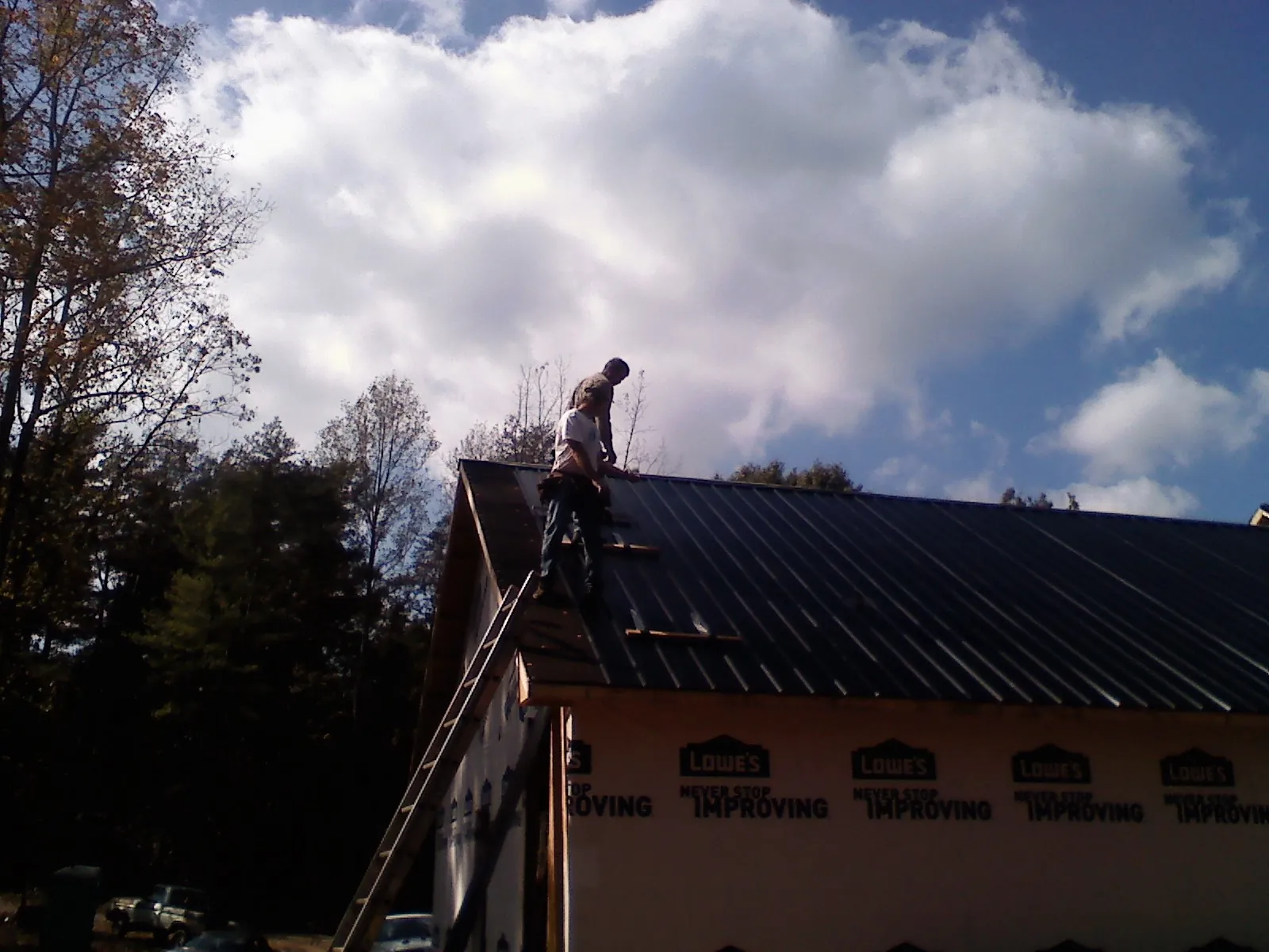 Roofer fastening dark metal panels high against a cloudy sky, from a Roof Inspection job in Antelope